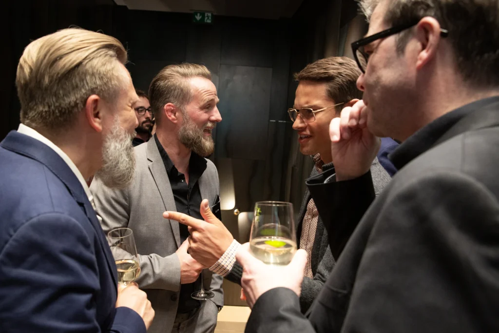 Vier Gäste im Gespräch, einer hält ein Glas Weißwein