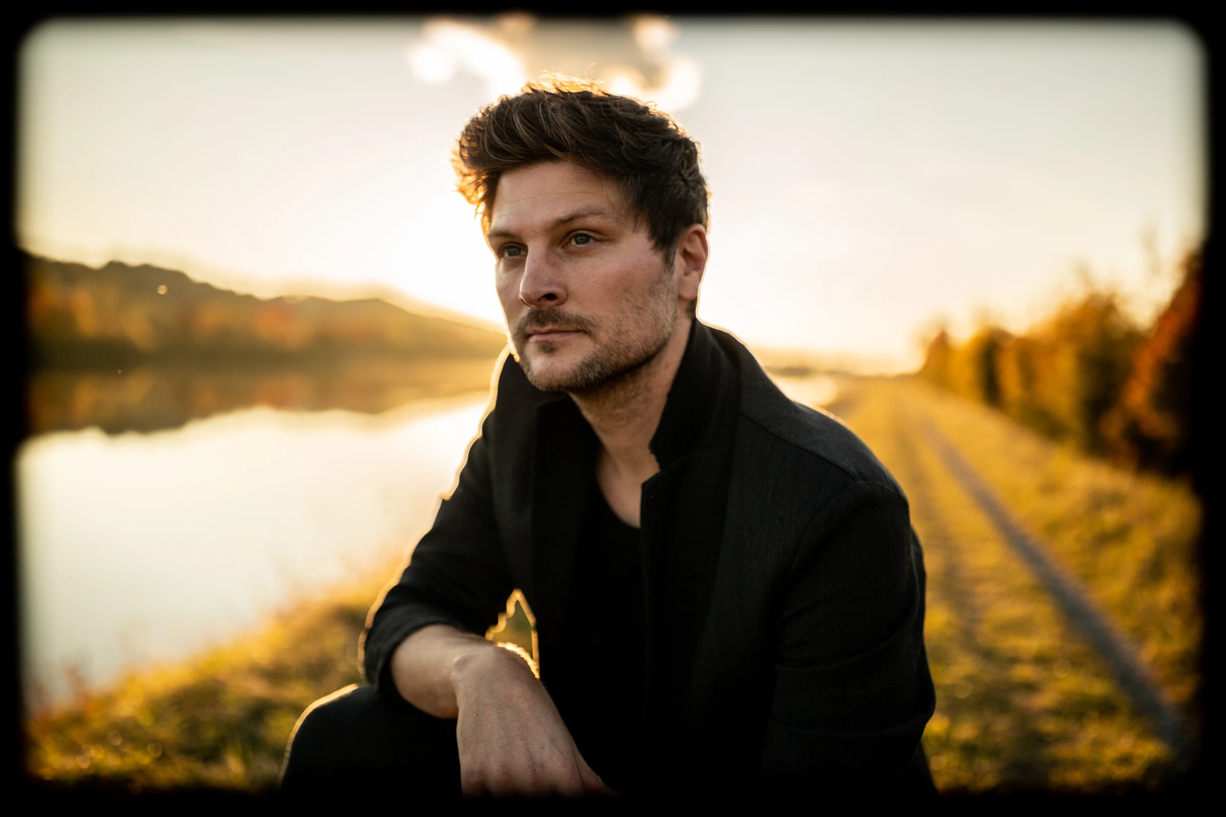 Anton Schröpfer in der Hocke am Ufer, rechts ein Weg im Abendlicht