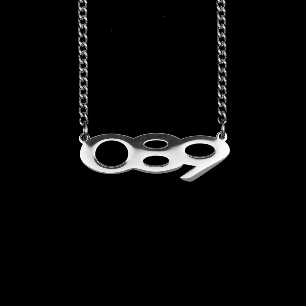 Silberne Kette mit dem Anhänger „089“ vor schwarzem Hintergrund
