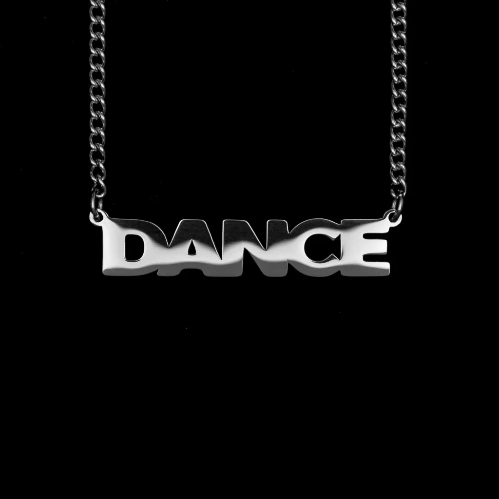 Silberne Kette mit dem Schriftzug-Anhänger „DANCE“ vor schwarzem Hintergrund