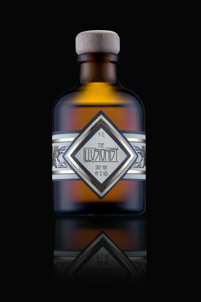 Flasche „The Illusionist Dry Gin“ aus braunem Glas mit Rautenetikett vor schwarzem Hintergrund
