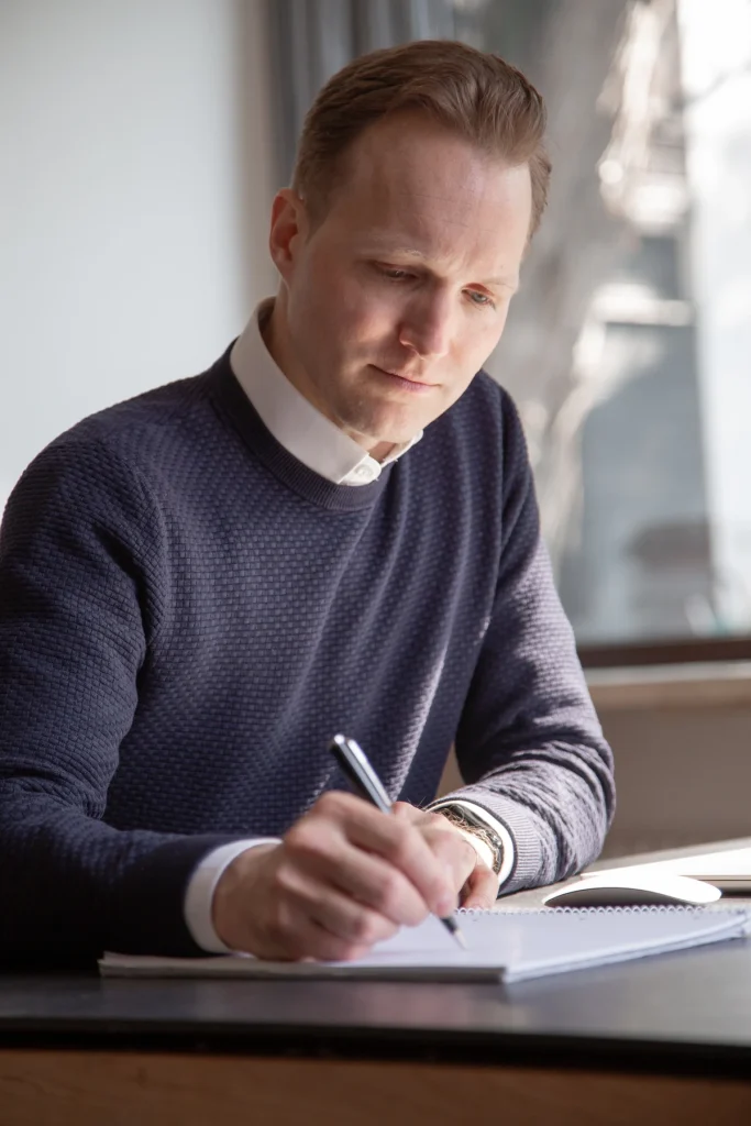 Johannes Rauch schreibt mit einem Stift in ein Notizbuch am Fenster