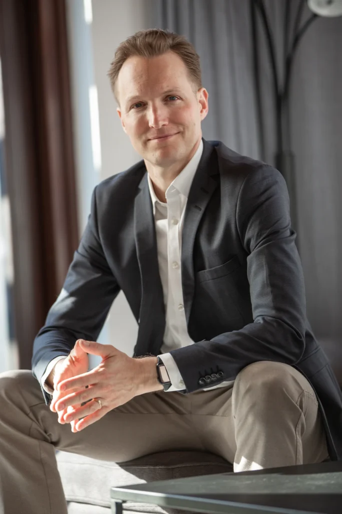 Johannes Rauch im Sakko sitzend, leicht zur Seite gedreht, die Hände gefaltet